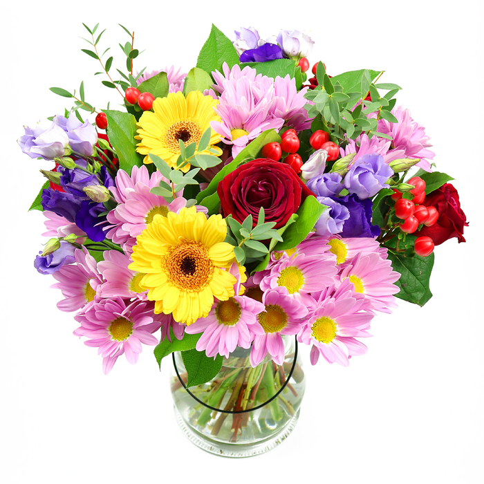 In this image, a lush mixed-colour bouquet is presented in a plain, cylindrical glass vase, placed against a clean white background that allows every bloom and leaf to stand out with clarity. At the centre, deep red roses unfurl their velvety petals, creating a core of rich, classic elegance that evokes heartfelt messages shared between friends and family across Dartmouth Park. Flanking them, bright yellow gerbera daisies glow with warm, sunlit energy, their dark brown-orange centres adding depth and contrast to their cheerful faces. Encircling these standout flowers, an abundance of soft pink daisies or chrysanthemums stretches outward, each with a ring of fine petals and a small yellow centre that contributes to the bouquet's plush, cushion-like fullness. Interspersed among the pink and yellow tones, slender stems of purple and lavender lisianthus rise gracefully, their bell-shaped, gently ruffled blossoms lending a cool, sophisticated note that feels as calming as the tree-lined streets near Chester Road. Sprays of vivid red hypericum berries peek out between petals, round and glossy, introducing a playful texture that breaks up the softer shapes. The entire composition is wrapped in layers of green foliage, from robust, darker leaves that frame the design to light, airy sprigs that add movement and a just-picked freshness. Through the transparent vase, the viewer can see the careful criss-cross of stems immersed in clear water, a testament to the florist's meticulous technique and respect for each stem. The bouquet feels perfect for a birthday, a thank-you gesture, or simply to brighten a living room overlooking Dartmouth Park, filling the space with colour, joy, and a sense of thoughtful care.